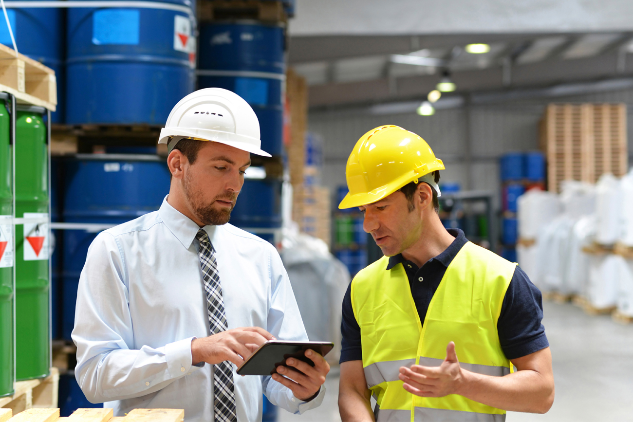 Two employees in chemical warehouse checking inventory levels on tablet device.